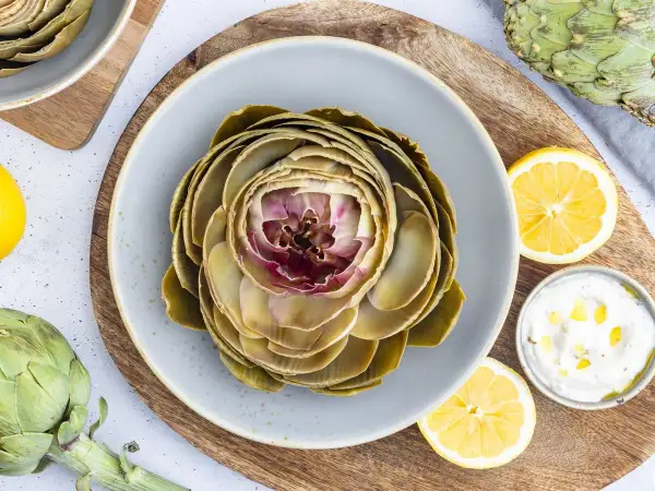 Gekochte Artischocke auf Teller, serviert mit Zitronenspalten und Dip. Perfekt für Artischocke Rezepte.